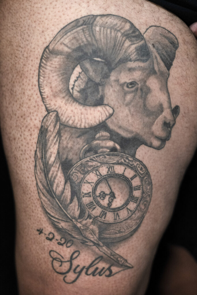 black and grey tattoo of a ram, stopwatch and a feather