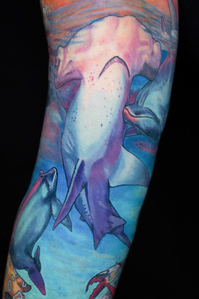 color realism tattoo of hammer head shark during sunset, lots of blues and pinks and purples,, dolphins in background, done by a Houston tattoo artist