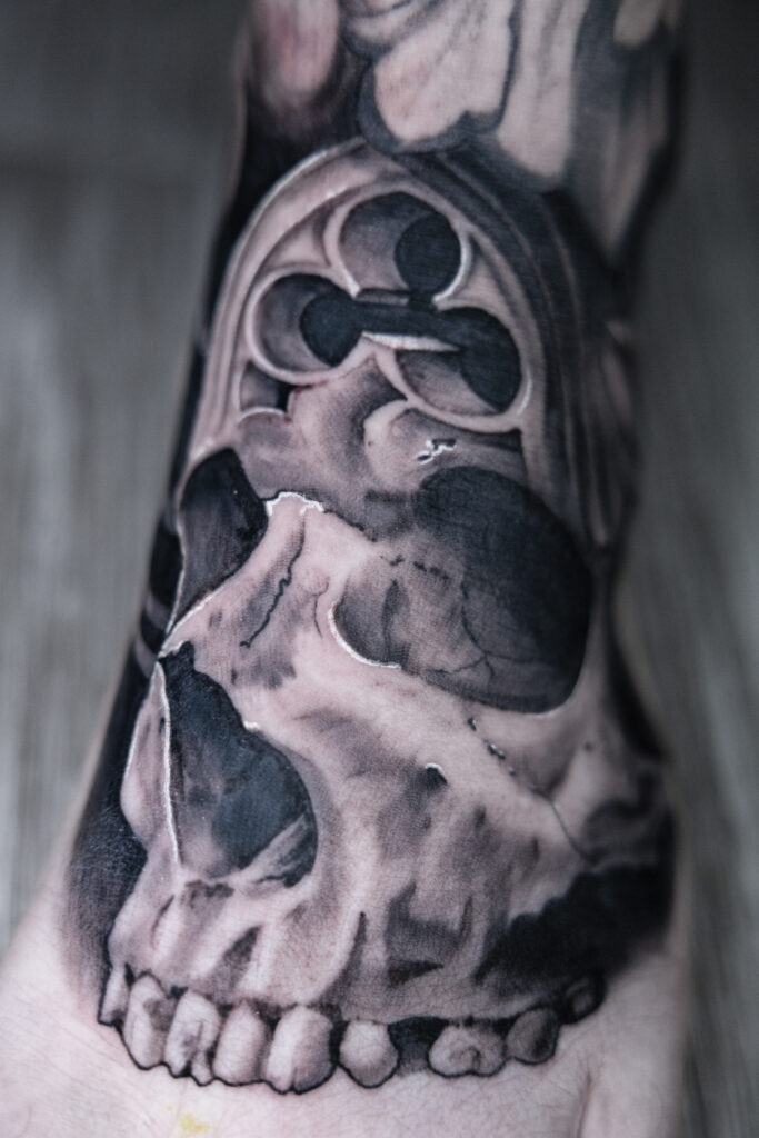black and grey foot tattoo done by a Houston tattoo artist, bishop effect on a skull and gothic architecture morph, textured skull with smooth architecture
