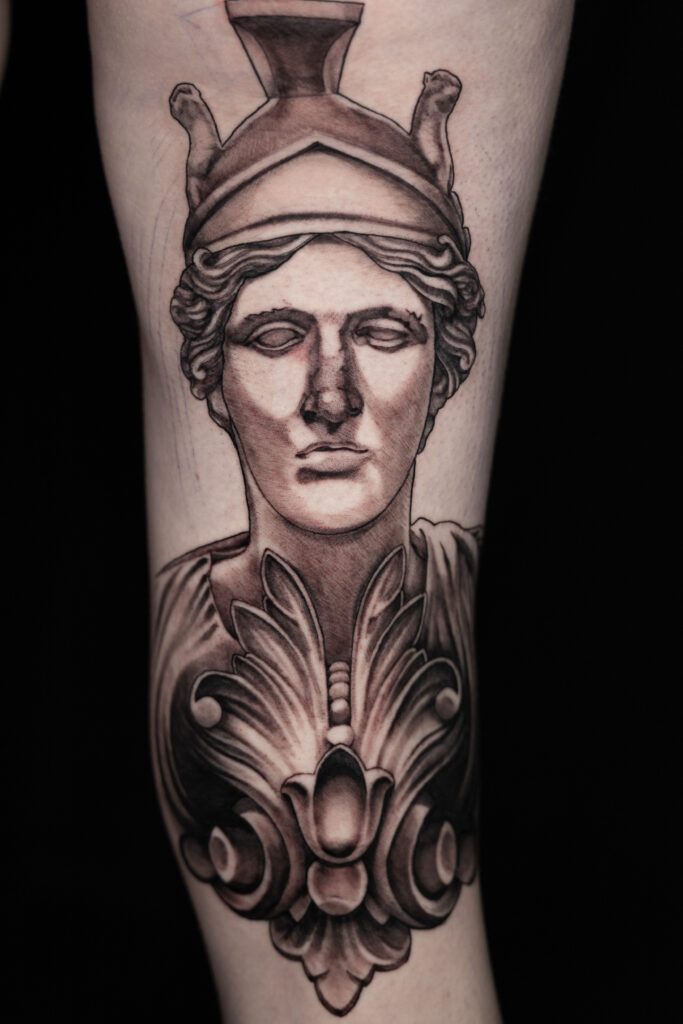 black and grey tattoo of a statuesque Athena behind the knee, with a large piece of filigree, smooth shading, done by a houston tattoo artist