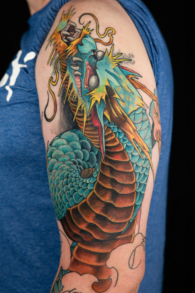 illustrative color realism coverup tattoo of a Japanese dragon, done on outer arm, teal scales with gold belly and spikes, done by Houston tattoo artist