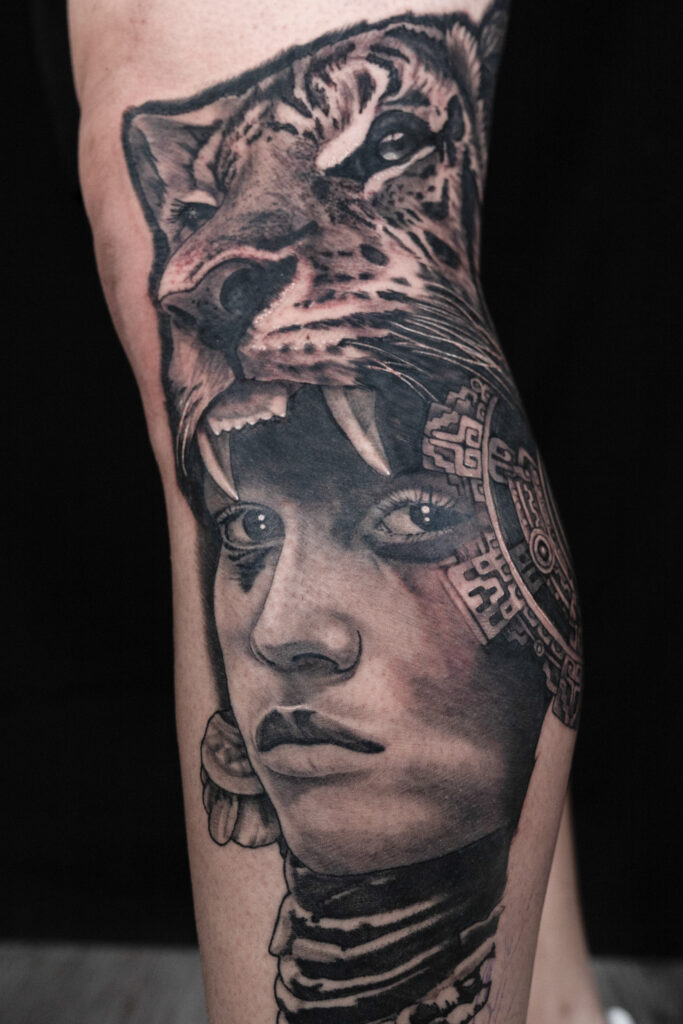 black and grey tattoo of an Aztec woman with a tiger headdress and a aztec symbol on fading into her face