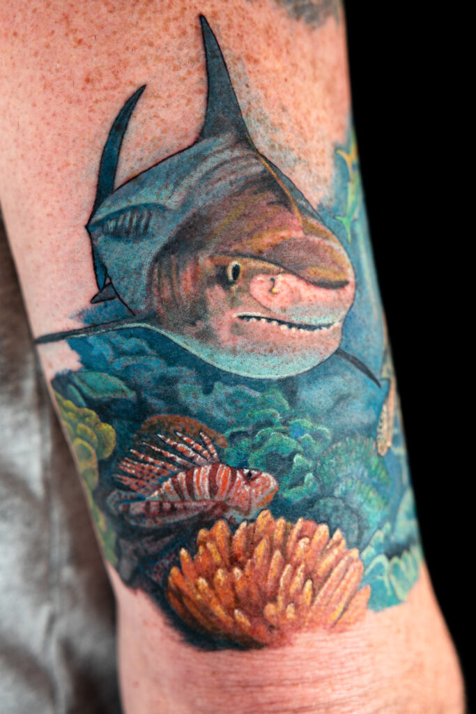 work in progress tattoo in full color realism on the arm, depicting a shark, lion fish, and coral, done by a Houston tattoo artist